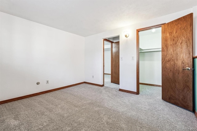 unfurnished bedroom featuring a closet, carpet flooring, a walk in closet, and baseboards