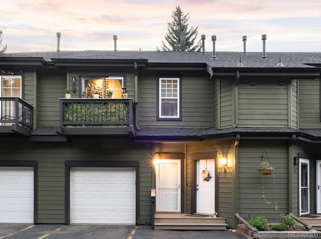 view of property featuring roof with shingles, driveway, a balcony, and an attached garage