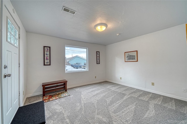 foyer entrance featuring baseboards, visible vents, a textured ceiling, and carpet