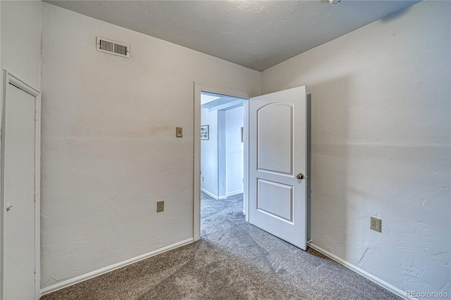 spare room with visible vents, carpet floors, baseboards, and a textured wall