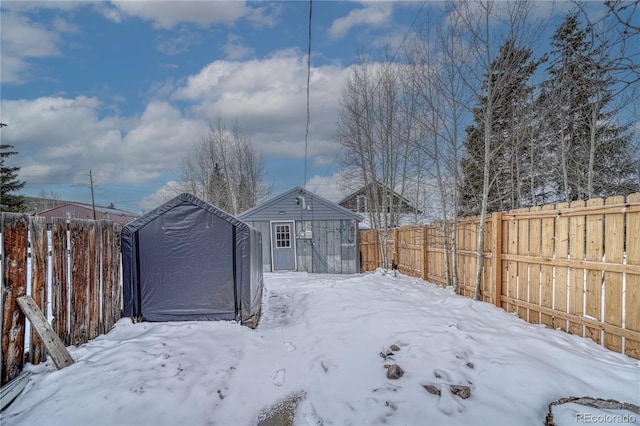 yard layered in snow with a fenced backyard, a storage unit, and an outdoor structure