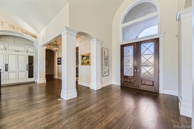 foyer with french doors, dark hardwood / wood-style flooring, high vaulted ceiling, decorative columns, and a chandelier