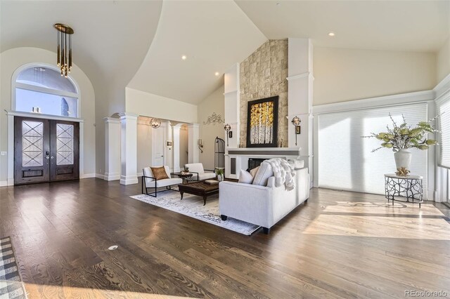 living room with a stone fireplace, ornate columns, and high vaulted ceiling