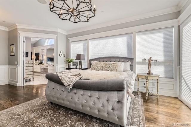 bedroom with connected bathroom, ornamental molding, wood-type flooring, and an inviting chandelier