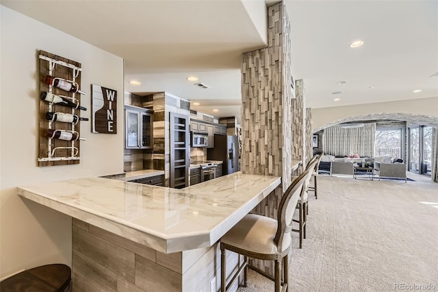 kitchen featuring kitchen peninsula, appliances with stainless steel finishes, light carpet, and a breakfast bar area