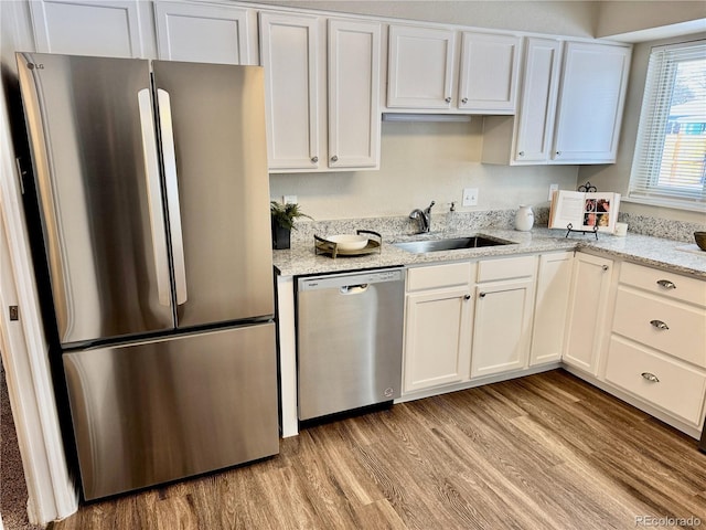 kitchen with sink, light stone counters, light hardwood / wood-style flooring, appliances with stainless steel finishes, and white cabinets