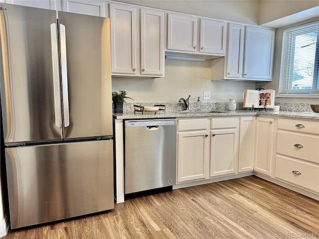 kitchen with light stone counters, light hardwood / wood-style flooring, white cabinets, and appliances with stainless steel finishes