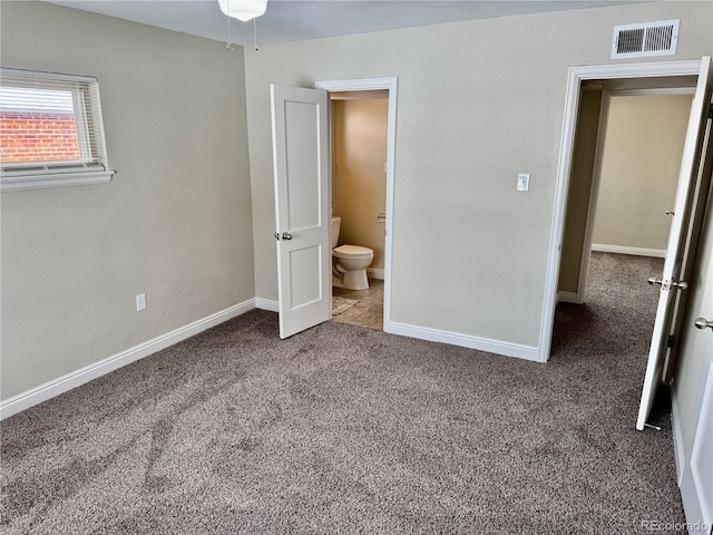 unfurnished bedroom with ensuite bathroom and dark carpet