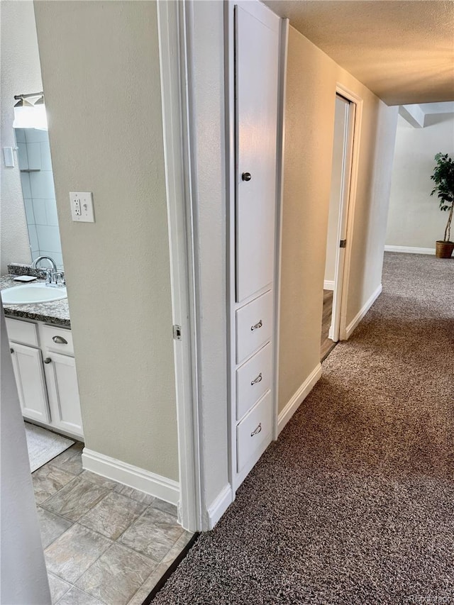 hall featuring sink, light colored carpet, and a textured ceiling