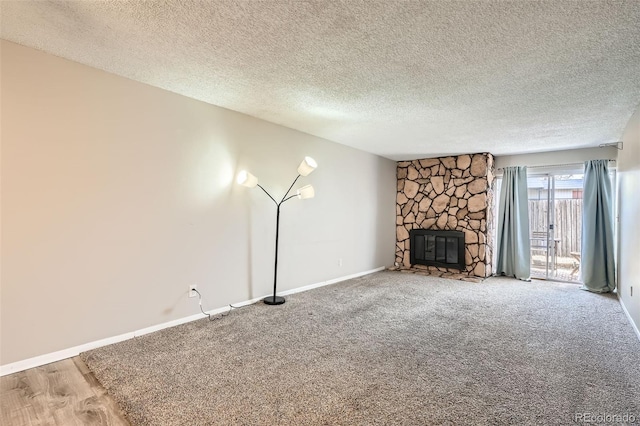 unfurnished living room featuring carpet, a stone fireplace, baseboards, and a textured ceiling