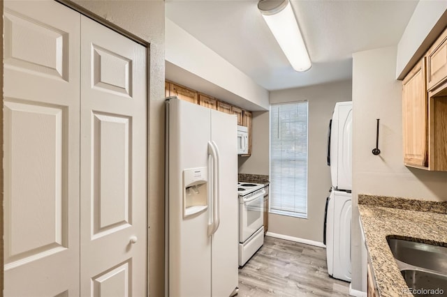 kitchen with white appliances, stone countertops, stacked washer and dryer, light wood-style floors, and a sink