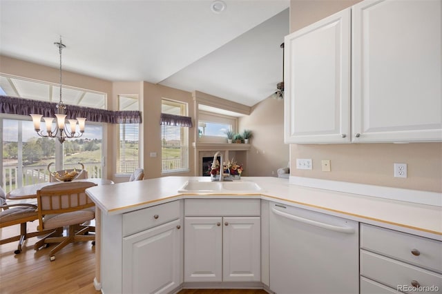 kitchen featuring white dishwasher, a sink, a peninsula, white cabinetry, and a chandelier