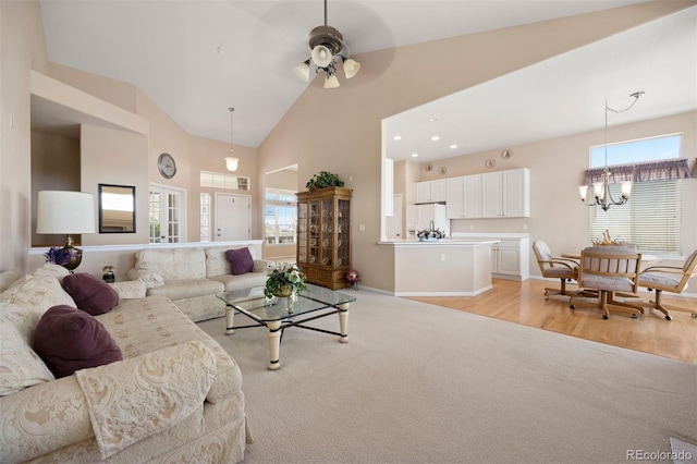 living room with a ceiling fan, plenty of natural light, high vaulted ceiling, a chandelier, and baseboards