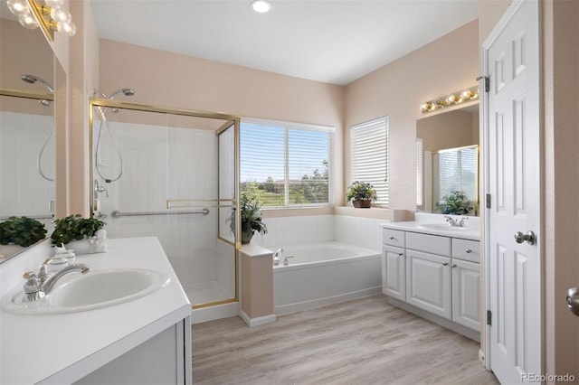 bathroom featuring a shower stall, a bath, two vanities, wood finished floors, and recessed lighting