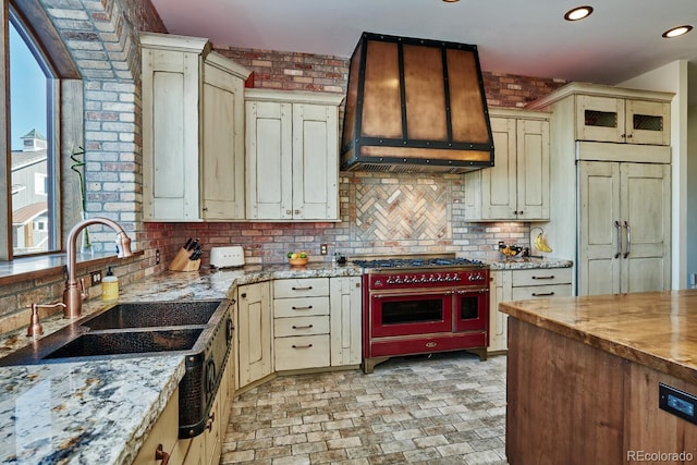 kitchen featuring custom exhaust hood, paneled built in fridge, cream cabinets, and range with two ovens