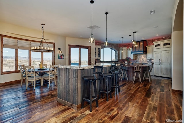 kitchen featuring light stone countertops, a kitchen bar, a large island with sink, and decorative light fixtures