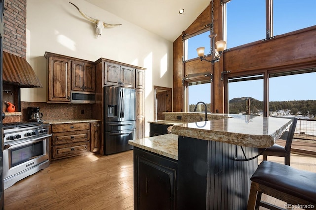 kitchen with a mountain view, high vaulted ceiling, tasteful backsplash, light stone counters, and stainless steel appliances