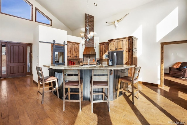 kitchen featuring light stone countertops, a breakfast bar, a barn door, high vaulted ceiling, and stainless steel fridge with ice dispenser