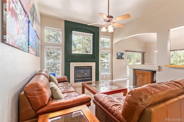 living room featuring a wealth of natural light, ceiling fan, a tiled fireplace, and high vaulted ceiling