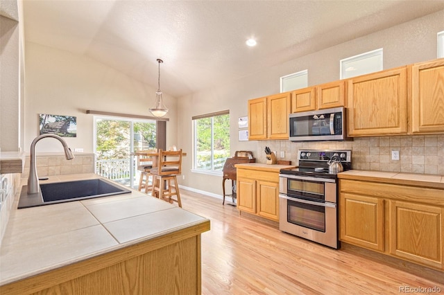 kitchen with light hardwood / wood-style flooring, decorative light fixtures, stainless steel appliances, sink, and vaulted ceiling