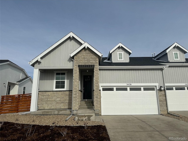 view of front of house featuring a garage, stone siding, concrete driveway, and fence