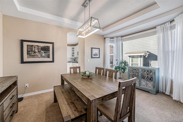 dining room with a raised ceiling and light colored carpet