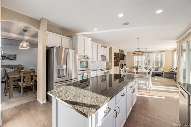 kitchen with appliances with stainless steel finishes, backsplash, dark stone countertops, white cabinets, and a center island