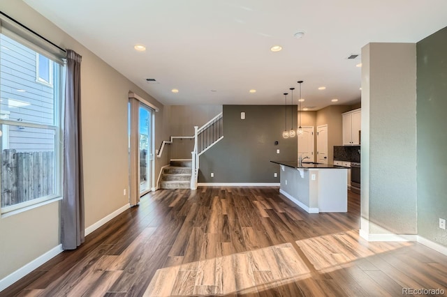 kitchen with white cabinets, dark hardwood / wood-style floors, hanging light fixtures, and an island with sink