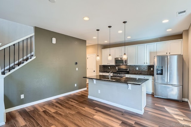 kitchen featuring white cabinets, a center island with sink, dark hardwood / wood-style floors, dark stone countertops, and appliances with stainless steel finishes