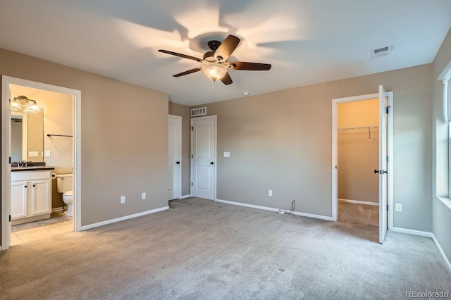 unfurnished bedroom featuring ensuite bathroom, a walk in closet, ceiling fan, light colored carpet, and a closet