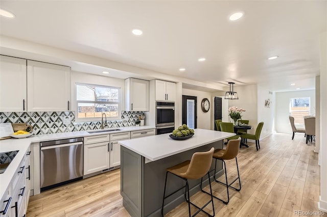 kitchen with appliances with stainless steel finishes, a kitchen bar, a sink, and light wood-style flooring