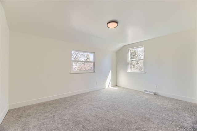 spare room with vaulted ceiling, carpet floors, visible vents, and baseboards