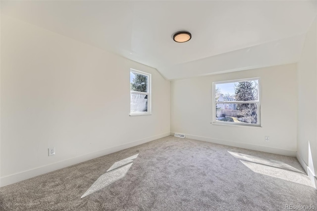 carpeted spare room featuring lofted ceiling, baseboards, and visible vents