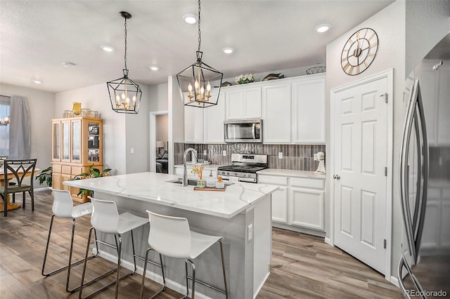 kitchen featuring light hardwood / wood-style flooring, hanging light fixtures, a center island with sink, white cabinetry, and appliances with stainless steel finishes