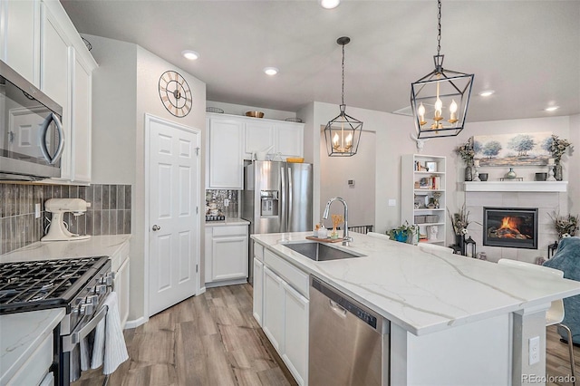 kitchen with sink, backsplash, stainless steel appliances, white cabinets, and a center island with sink