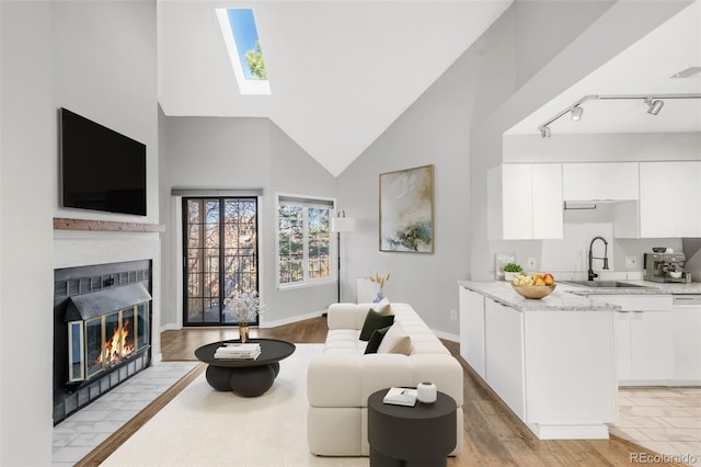 living room with a skylight, sink, high vaulted ceiling, track lighting, and light wood-type flooring