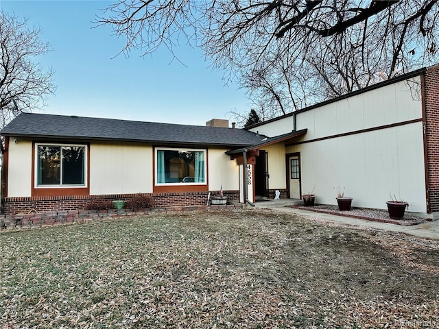 view of front of property with brick siding, a front lawn, and a shingled roof