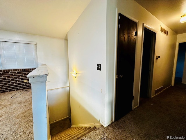 corridor with brick wall, visible vents, carpet flooring, and an upstairs landing