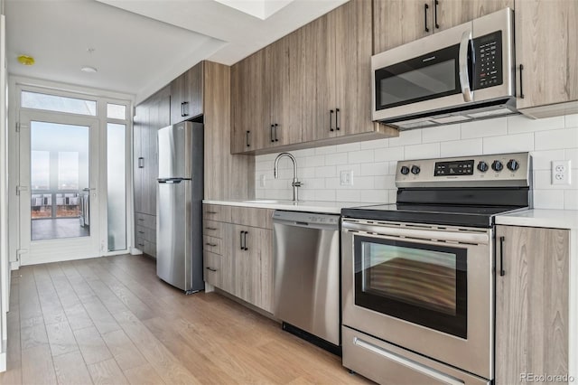 kitchen with light wood-style flooring, a sink, backsplash, stainless steel appliances, and light countertops