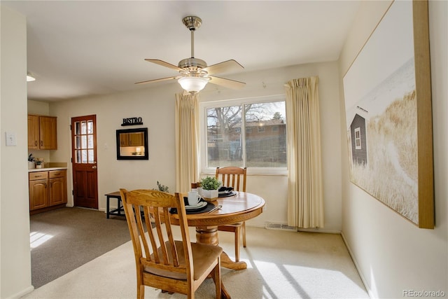 dining area with baseboards, light colored carpet, visible vents, and ceiling fan