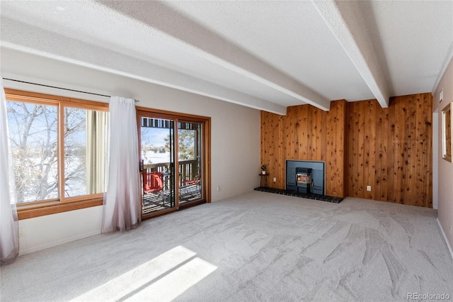 unfurnished living room featuring wooden walls, a wood stove, carpet floors, a textured ceiling, and beam ceiling