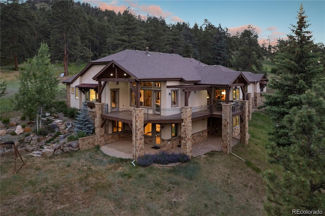 back of house at dusk featuring a patio, stucco siding, a lawn, stone siding, and stairs