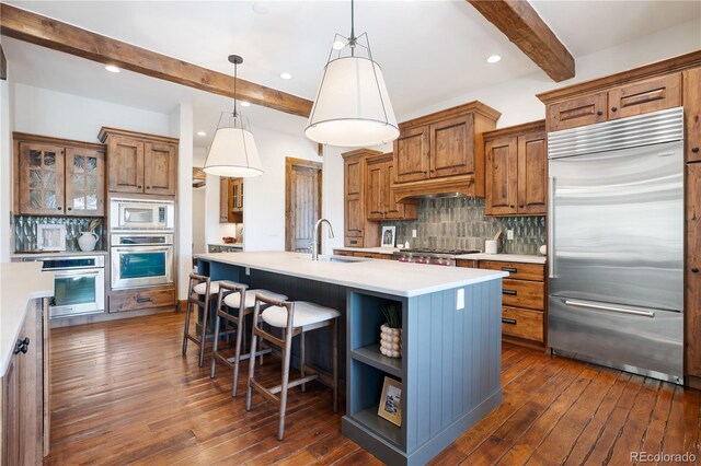 kitchen with a kitchen island with sink, built in appliances, backsplash, dark hardwood / wood-style flooring, and beam ceiling