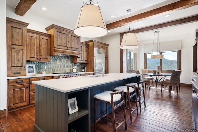 kitchen featuring appliances with stainless steel finishes, sink, premium range hood, an island with sink, and dark wood-type flooring