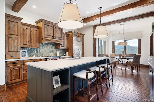 kitchen featuring a center island with sink, custom range hood, appliances with stainless steel finishes, brown cabinets, and a sink