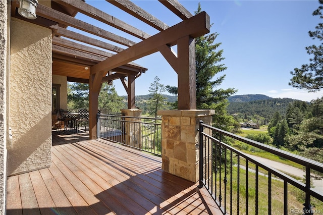 wooden terrace featuring a wooded view, a mountain view, and a pergola