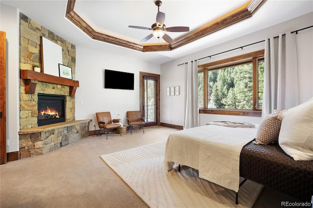 bedroom with carpet floors, access to exterior, crown molding, a raised ceiling, and a stone fireplace