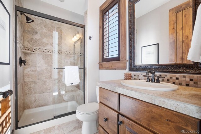 bathroom with toilet, tile patterned floors, vanity, backsplash, and a shower with shower door