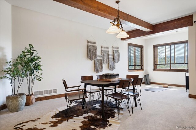 carpeted dining space with beamed ceiling