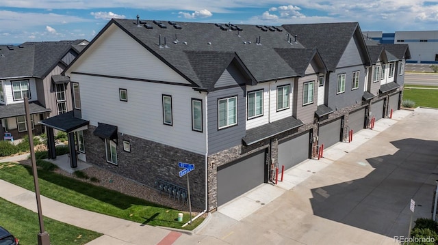 9250 Garnett Way Unit D, Arvada, CO 80007 - view of home's exterior featuring stone siding, an attached garage, driveway, and a shingled roof